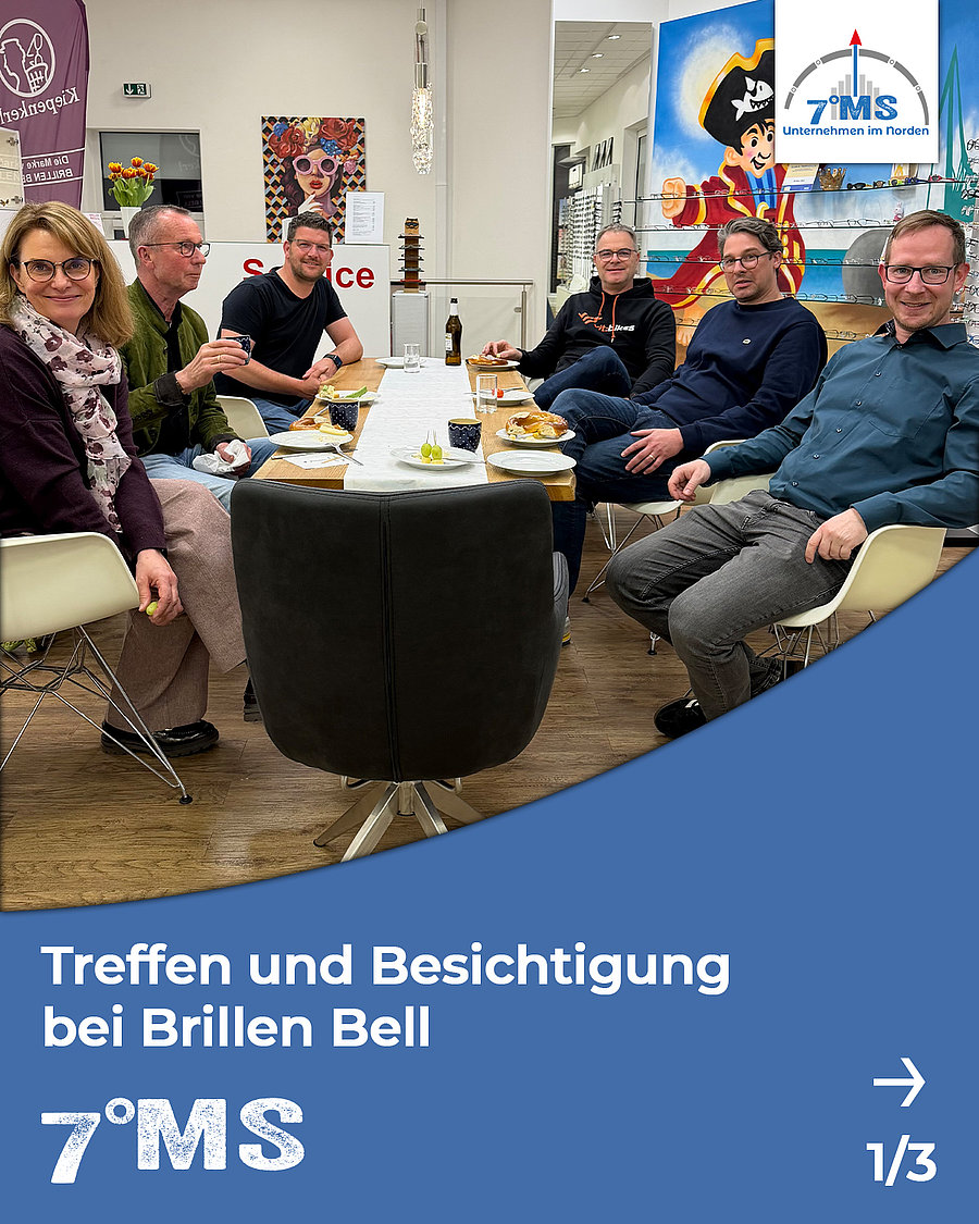 Bildbeschreibung: Eine Gruppe von sechs Personen sitzt an einem Tisch und genießt eine Mahlzeit. Es findet ein Treffen und eine Besichtigung bei "Brillen Bell" statt. Im Hintergrund sind verschiedene Kunstwerke und ein Regal mit Brillen zu sehen.